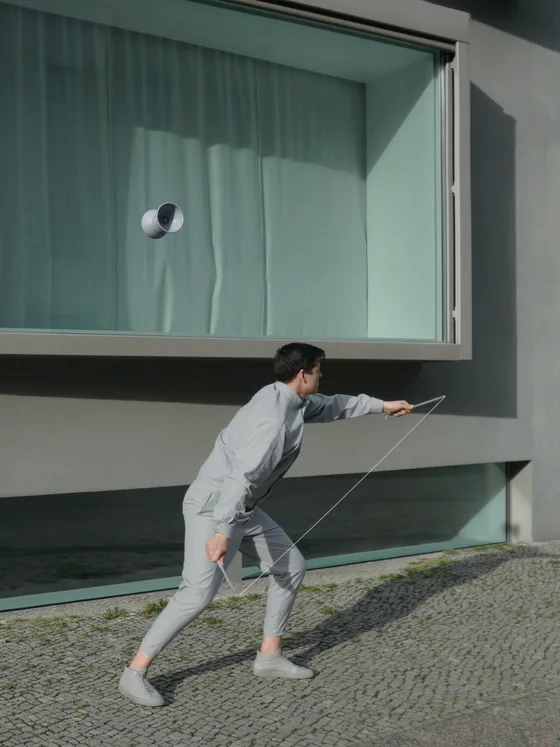 A diabolist in grey leans into a throw on cobblestones, the diabolo suspended in the air against a concrete building’s window.